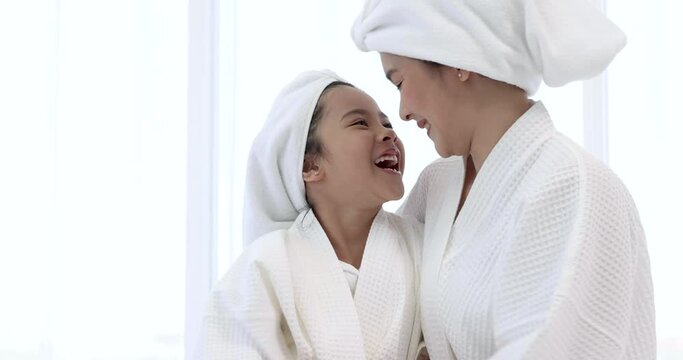 Mother and daughter in white bathrobes are having fun spa treatments.