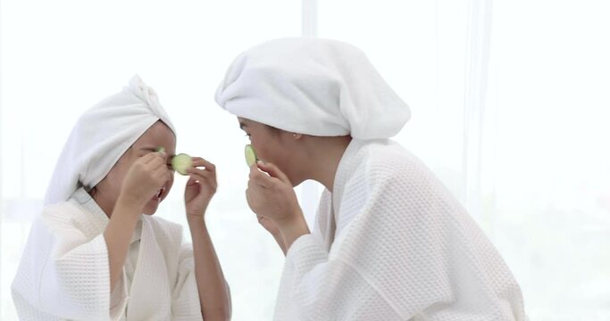Mother and daughter in white bathrobes are having fun spa treatments.