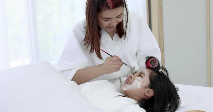 Mother and daughter in white bathrobes are having fun spa treatments.