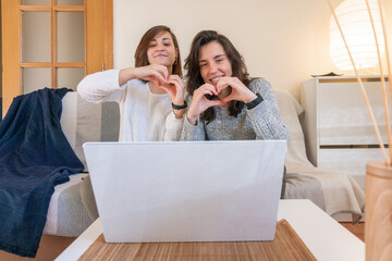 Smiling lesbian couple sitting on sofa and making a video call with a laptop