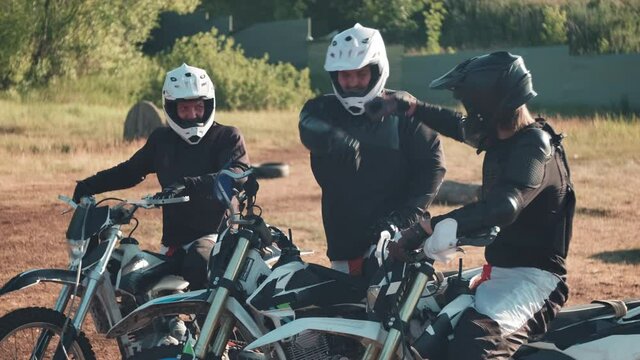 Slowmo medium shot of cheerful three men in gear and helmets sitting on motorcycles outdoors and fist bumping each other before going for ride