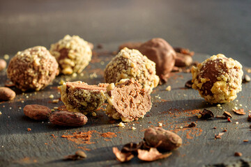 Handmade chocolates sprinkled with pistachio crumbs and cacao beans on a graphite board photographed in close-up