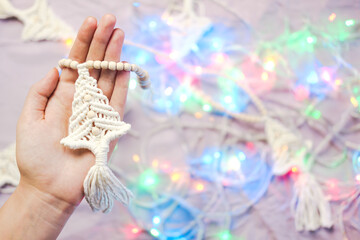 Handmade crochet new year decoration in woman hands. Person holds a christmas garland in the shape of fir tree. Decorating home for winter holidays concept, copy space