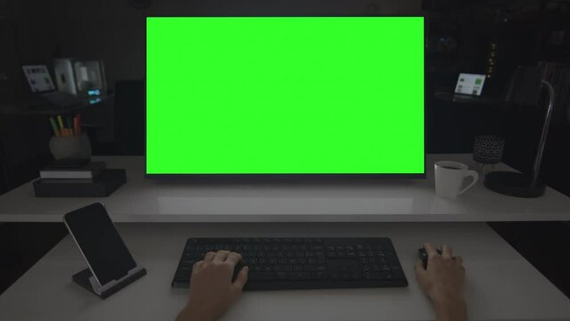 Desktop computer with green screen. Big dark room with several devices. Evening in the office or home office. Chroma key. Perfect to put your own images or videos. Track with perspective corner pin.