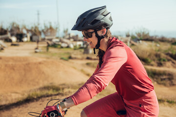 Sportswoman in black helmet and red sportswear with glasses riding mountain bike on training track