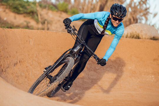 Sportswoman in black helmet and blue sportswear with glasses riding mountain bike on training track
