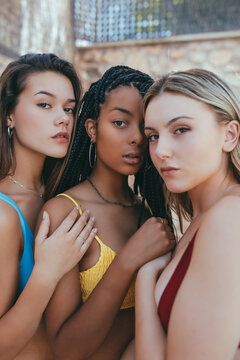 Tranquil multiethnic females wearing bikini bras standing close to each other and looking at camera