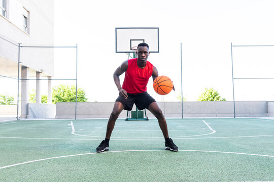 Serious African American male playing basketball on modern sports ground and looking at camera during training