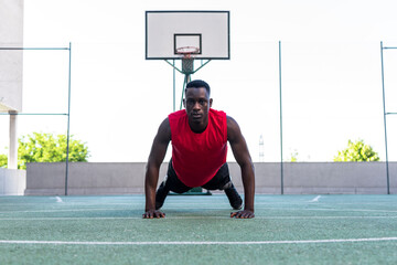 Determined black male basketball player doing push ups during intense training on sports ground and looking at camera