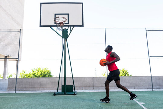 Side view of African American sportsman jumping while playing basketball during training and throwing ball into hoop