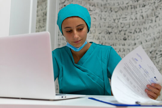 Crop unrecognizable nurse sitting at table and handwriting on clipboard while preparing medical report during work in hospital