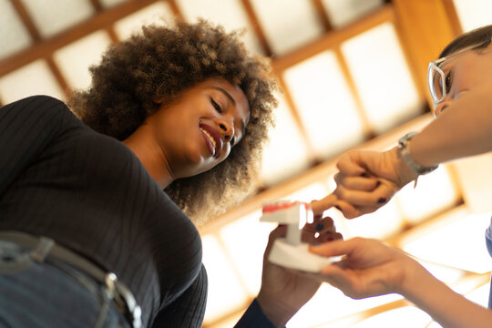 Low angle view of cheerful African American lady talking with Caucasian female dentist about teeth implants in dental clinic