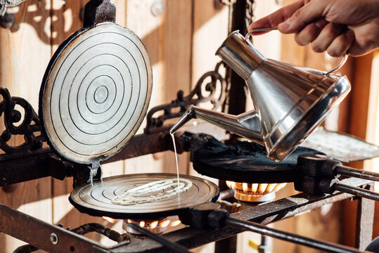 Crop Anonymous Person Pouring Liquid Dough From Metal Kettle On Waffle Iron Placed On Gas Stove While Preparing Typical Catalan Neula Biscuits In Kitchen