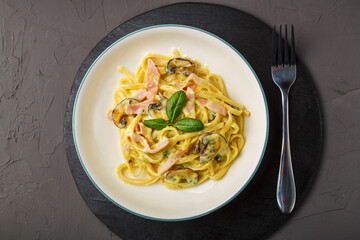 a plate of pasta with ham and mushrooms in a creamy basil sauce on a black round stand with a fork.