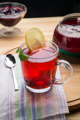 Berry tea in a cup with lemon on a napkin next to a spoon.