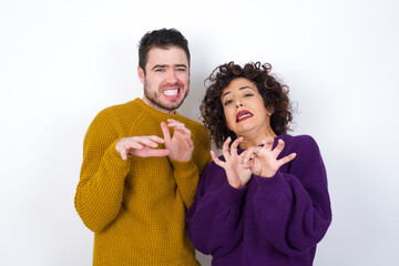 Ugh how disgusting! Displeased Young couple wearing knitted sweater standing against white wall,...