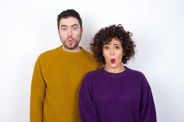 Young couple wearing knitted sweater standing against white wall expressing disgust, unwillingness,...