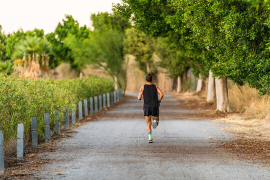 Back view of unrecognizable sportive male athlete in activewear running along path in park during cardio workout in summer