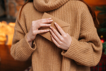 Close-up view of unrecognizable young woman wearing winter sweater holding in hands paper envelope...