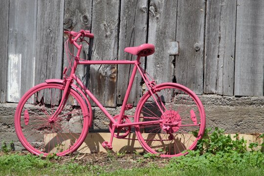old bicycle painted pink beside barn