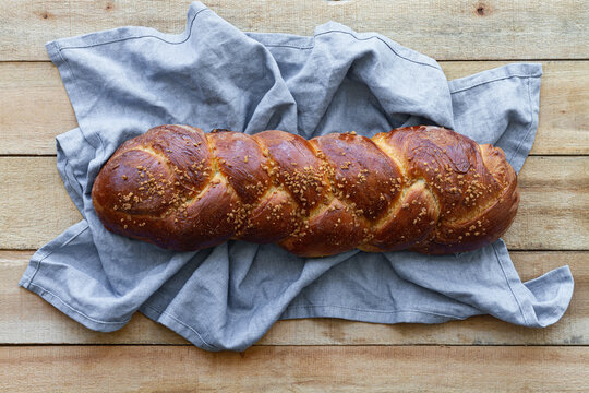 Top view of appetizing aromatic braided bread with seeds placed on linen napkin on wooden table