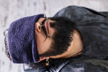High angle of crop unrecognizable male with styling mustache and brutal bearded man with piercing during haircut procedure in barbershop