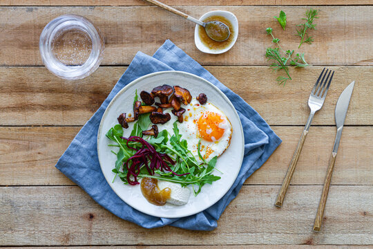 Top view of plate with palatable fried egg served with mushrooms and fresh salad on wooden table with sauce and glass of water