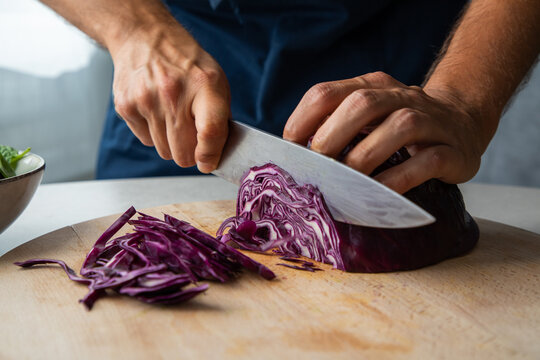 Crop anonymous cook chopping fresh natural red cabbage on wooden cutting board while preparing healthy dish in kitchen