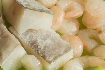 Close-up of some delicious raw cod fillets with ice glaze accompanied by some thawed prawns. Fish and seafood meat.
