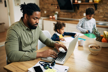 African American single father working on laptop at home.