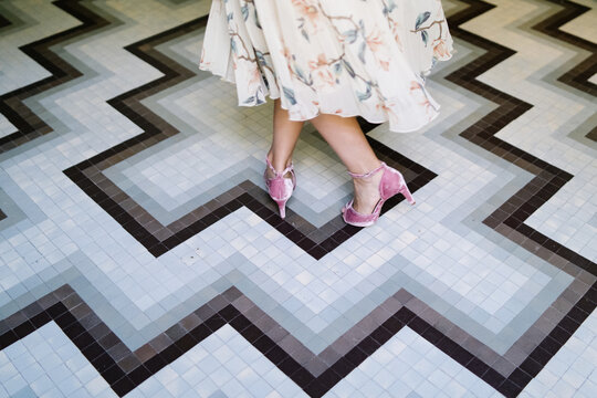 High angle of unrecognizable female wearing elegant dress and stylish high heeled shoes turning around on floor in luxury boutique