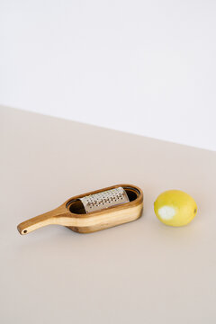 Fresh whole lemon arranged on table with sharp wooden grater in studio on two colored background