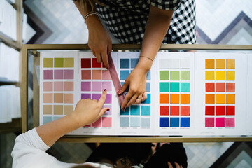 Top view of unrecognizable female designers standing at table in bright studio and choosing color of textile samples