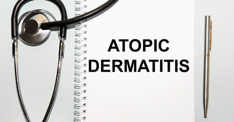 In the notebook is the text OF ATOPIC DERMATITIS, next to the stethoscope and pen.