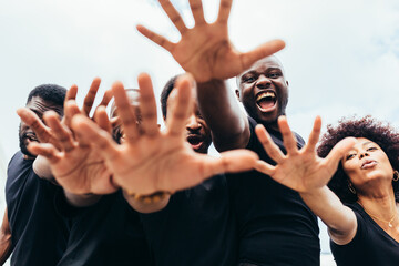 Cheerful black men and woman raising hands against a blue sky