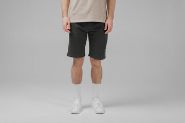 a man without a face stands on a gray background in a T-shirt, shorts, sneakers, white socks