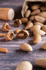 
Ecological split almonds with their fruit outside, raffia bag with almonds scattered on a wooden table, wooden mallet to split the almonds. Selective focus