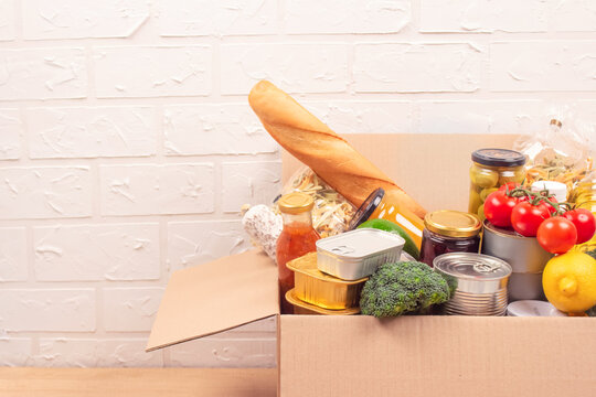 Donation box with different groceries, food donations on light background with copyspace - pasta, fresh vegatables, canned food, baguette, cooking oil. Food bank, food delivery concept