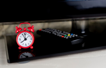 TV set-top box remote and red alarm clock, depending on the TV