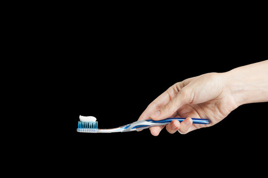 Hand Of A Woman Holding Toothbrush With Toothpaste Isolated On Black Background. Female Hand With Blue Tooth Brush