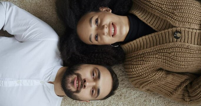 Top view of multiethnic multinational loving couple lying on floor relaxing talking enjoying spending time together. Male caucasian happy face and female african american head looking at camera smiles