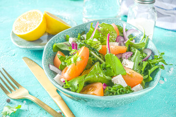 Bowl of healthy vegetable salad with various leaf salad, tomatoes, feta cheese, onions, olive oil, light blue concrete background copy space