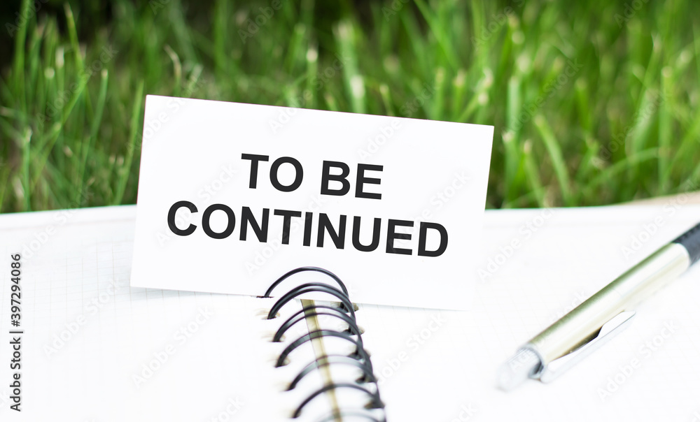 Poster text to be continued on a white card that lies on an open notebook on the table, next to the pen.