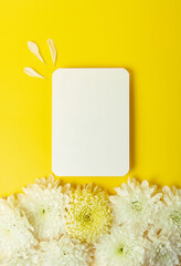 Blank white card on the bold yellow background with beautiful chrysanthemums on the background.Mockup for design.Vertical photography with copy space.