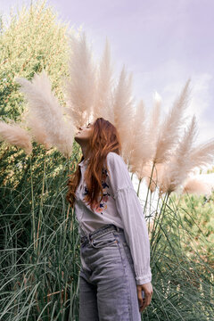 Young redhead woman standing by pampas grass in garden