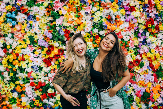 Cheerful beautiful female friends standing against colorful flowers