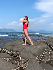 woman in red swimsuit standing on the beach stones