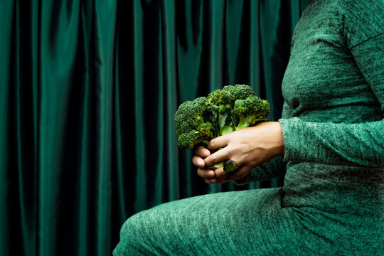 Midsection of woman holding broccoli while sitting by green curtain