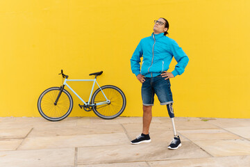 Man with artificial limb and foot standing with hand on hip against yellow wall