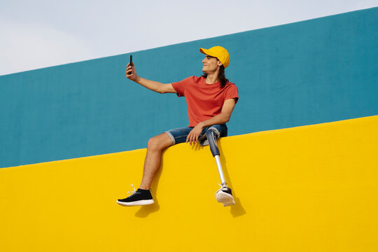 Smiling man taking selfie while sitting on multi colored wall